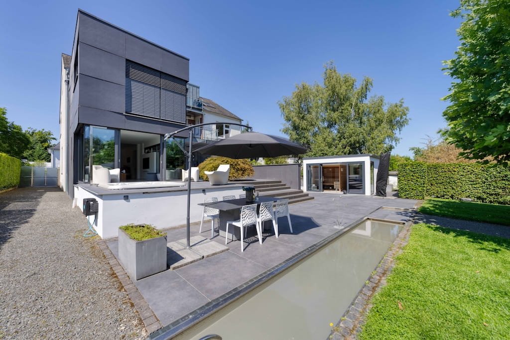 Die Außenansicht einer Luxusimmobilie in Trier mit Terrasse, Wasserbecken und Gartenanlage.