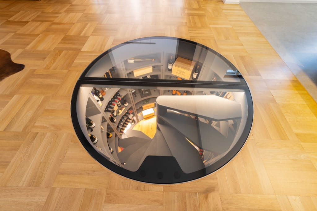 Ein Weinkeller einer Luxusimmobilie in Trier mit Wendeltreppe, sichtbar durch einen runden Glasboden im Wohnbereich.