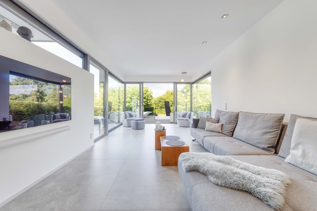 Ein lichtdurchflutetes Wohnzimmer einer Luxusimmobilie in Trier mit großer Fensterfront.